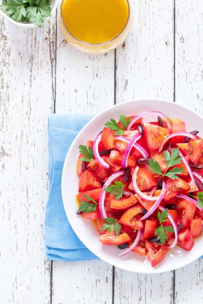 round plate holding Tomato Salad, with Cumin Dressing and fresh parsley on the side