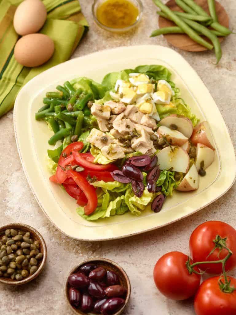 Offwhite plate showing one portion of Tuna Salad Nicoise recipe, with ingredients surrounding the plate