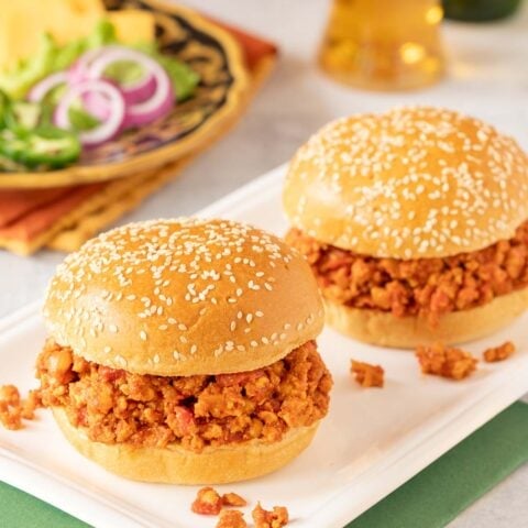 two turkey sloppy joes on a white platter with toppings and a beer in the background