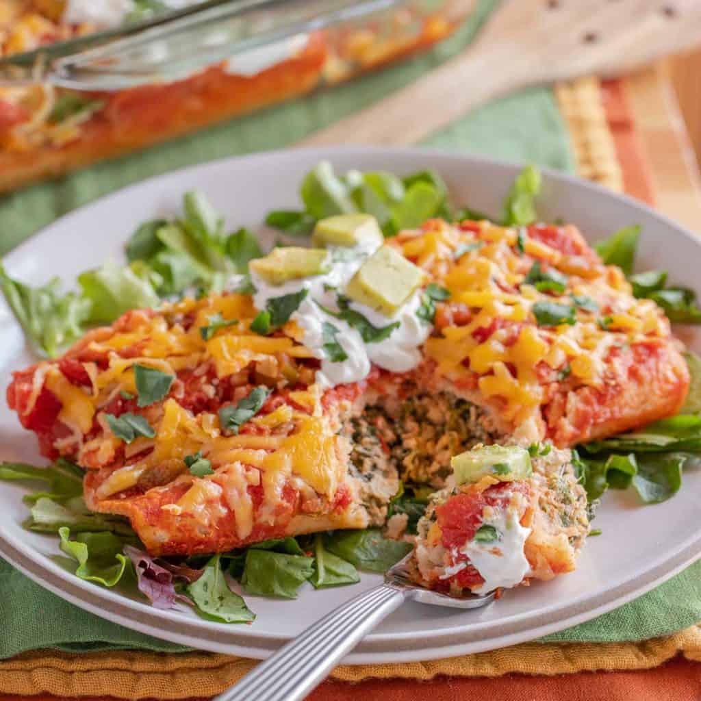 White plate with a serving of Turkey Spinach Enchiladas, with one bite on a fork
