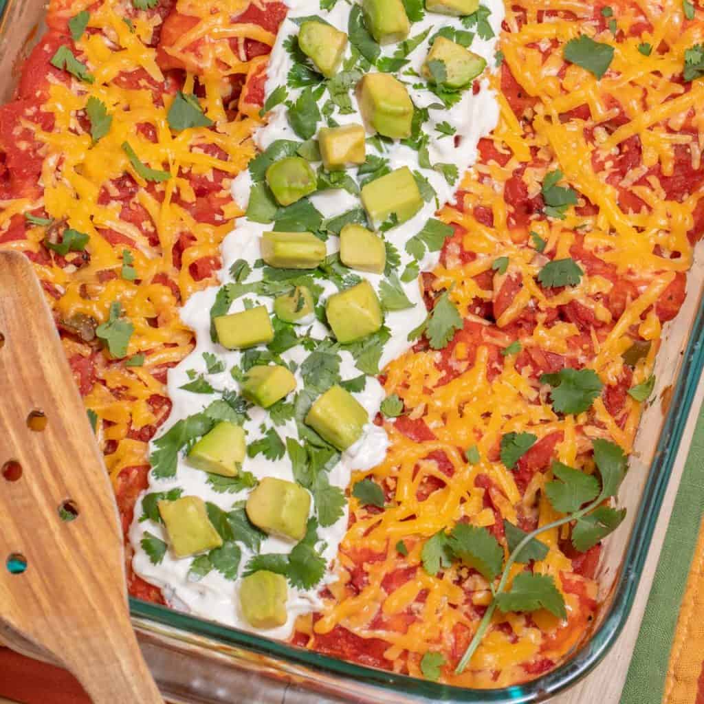 Pyrex dish filled with Turkey Spinach Enchiladas and garnished with sour cream, cilantro and avocado