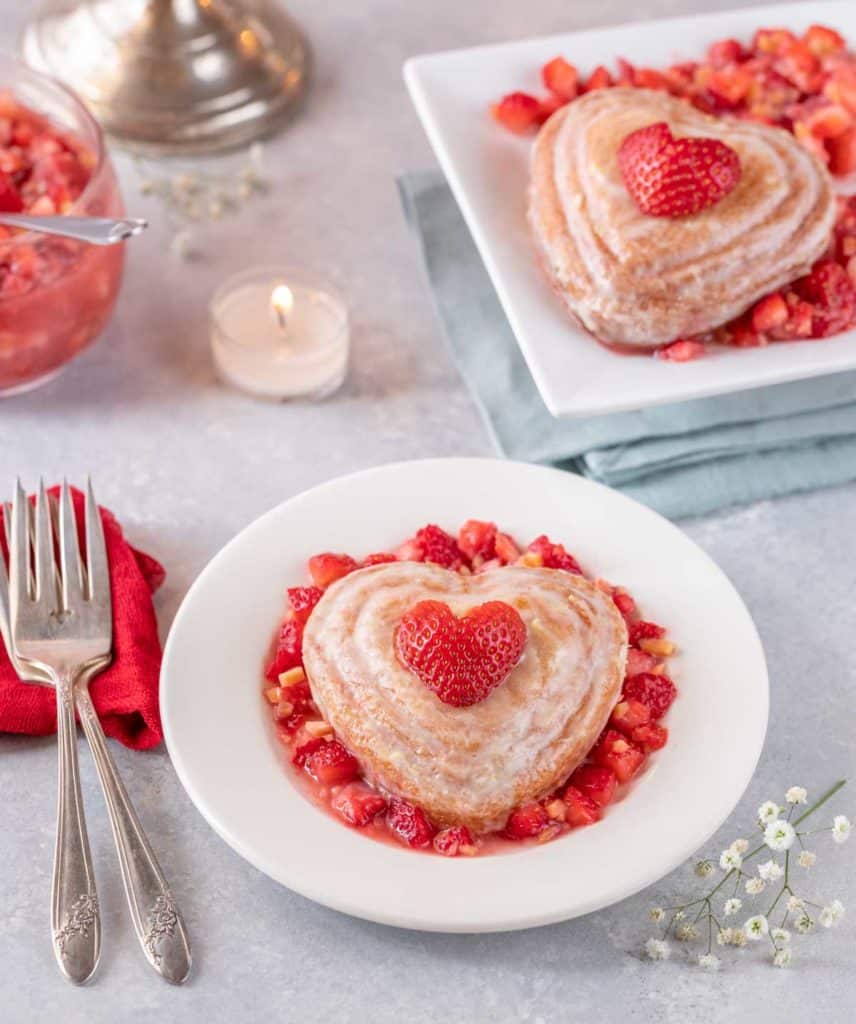 Round white plate holds a single Valentine's mini cake with strawberry almond salsa. A second portion is on a plate in the background.