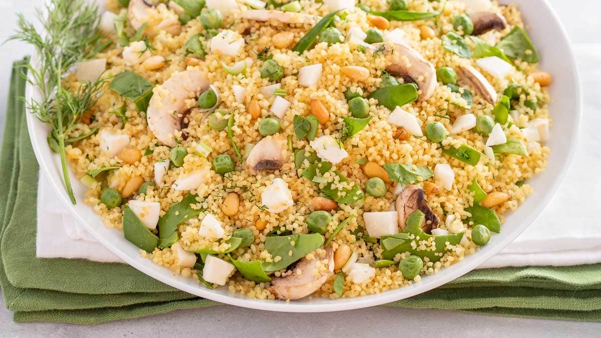 close up of vegetable couscous salad in a white bowl, showing various ingredients, colors, and textures.