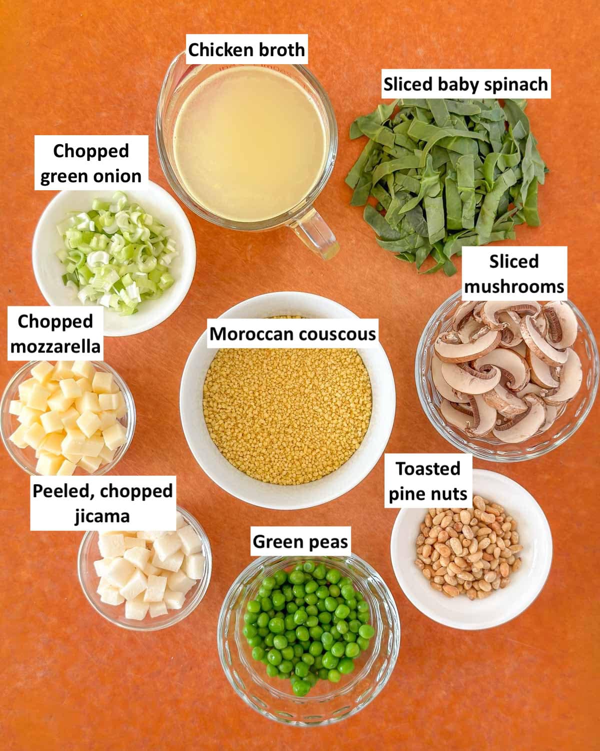 Ingredients for vegetable couscous salad on a cutting board, prepped and labeled.
