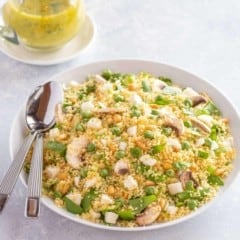 white bowl holding vegetable couscous salad, with 2 spoons on the side and dill vinaigrette in the back.