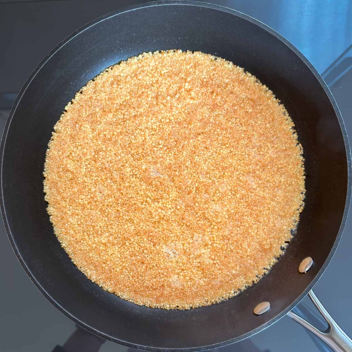 Chicken broth added to toasted couscous in a skillet.