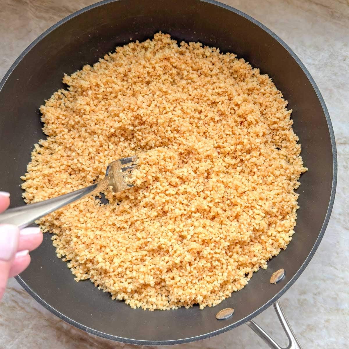 Fluffing cooked couscous with a fork after it has absorbed the broth.