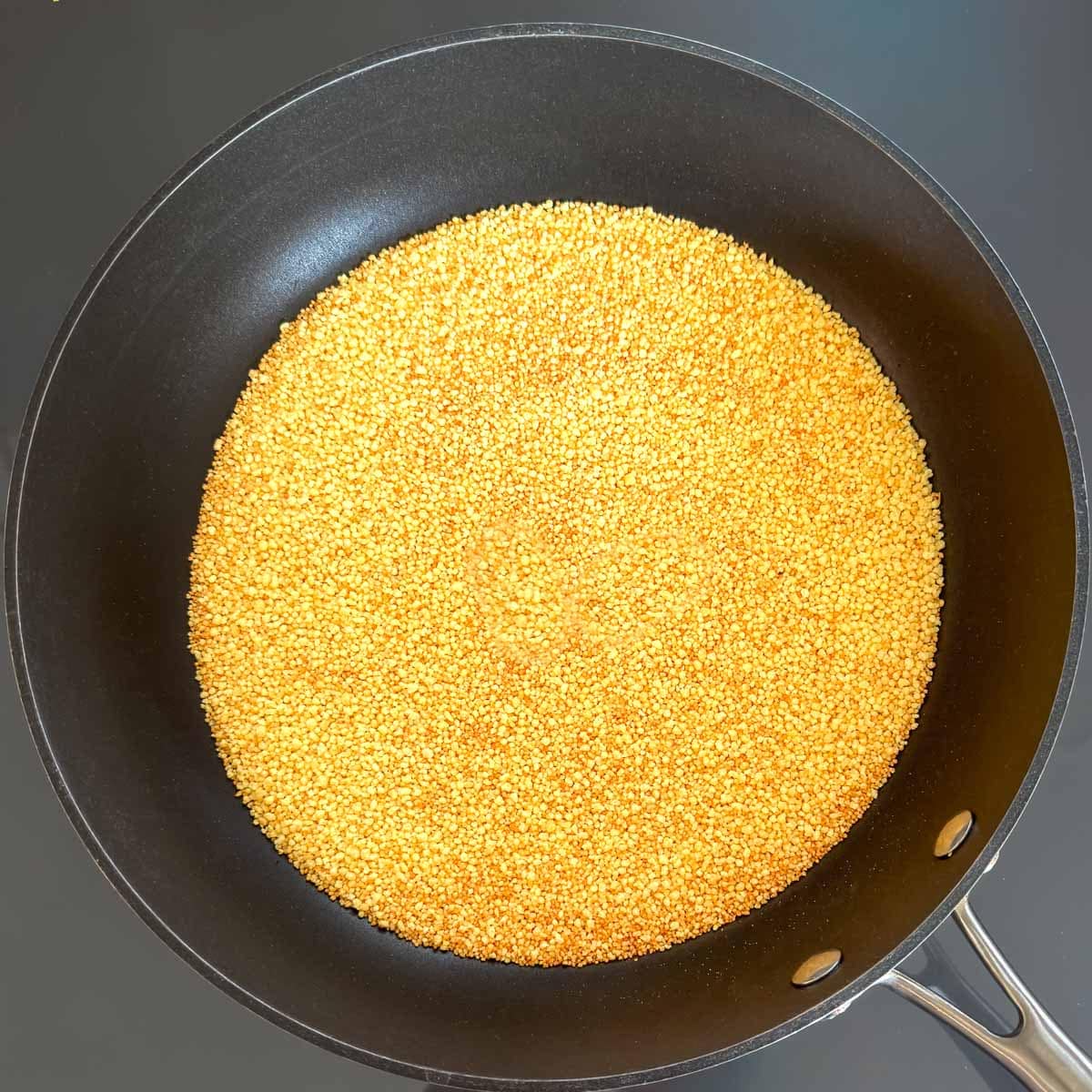 Moroccan couscous toasting in a skillet until lightly browned.