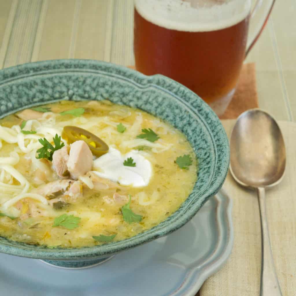 White Bean and Chicken Chili in a blue bowl with a mug of beer