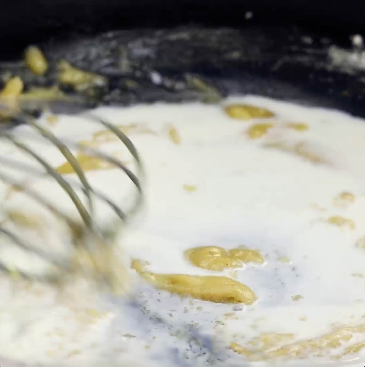 process shot showing whisking milk into roux of butter and flour